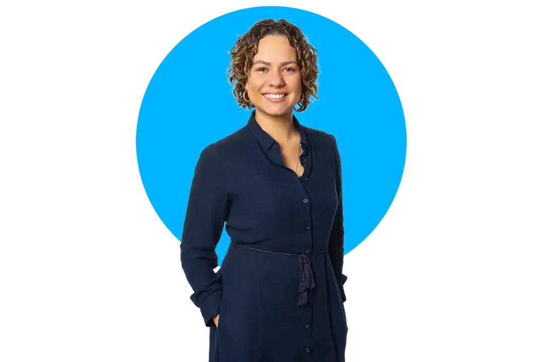 Hollie-anna King smiling with curly hair in a blue dress stands in front of a large blue circle background