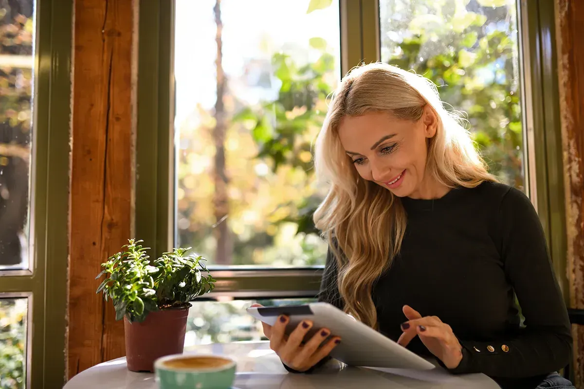 mature woman looking at her conveyancing quote on a tablet sitting in the window of the house she's recently sold using Upstix