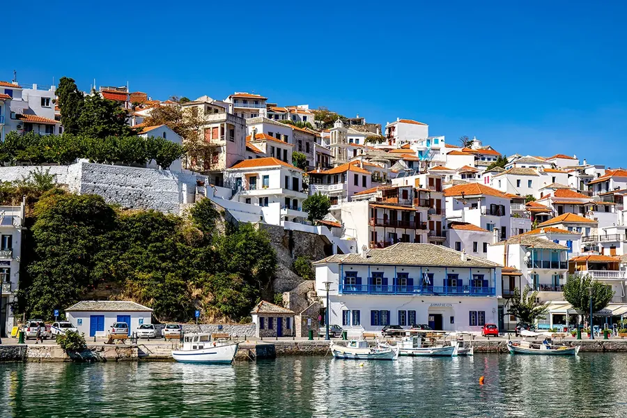 view of the beautiful small harbour on the greek island of Skopelos where Villa Donna from the film Mamma Mia is situated. Cluster of white greek villas with orange roofs looking out onto the harbour with a clear blue sky and calm sea