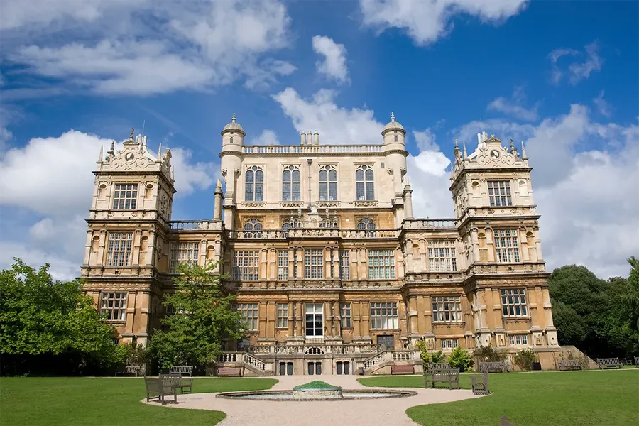 front view of wollaton hall in the east midlands. A huge stately home with a turret either side and large steps going up to the front entrance on both sides of the house. It was used as the location of wayne manor in one of the batman films.