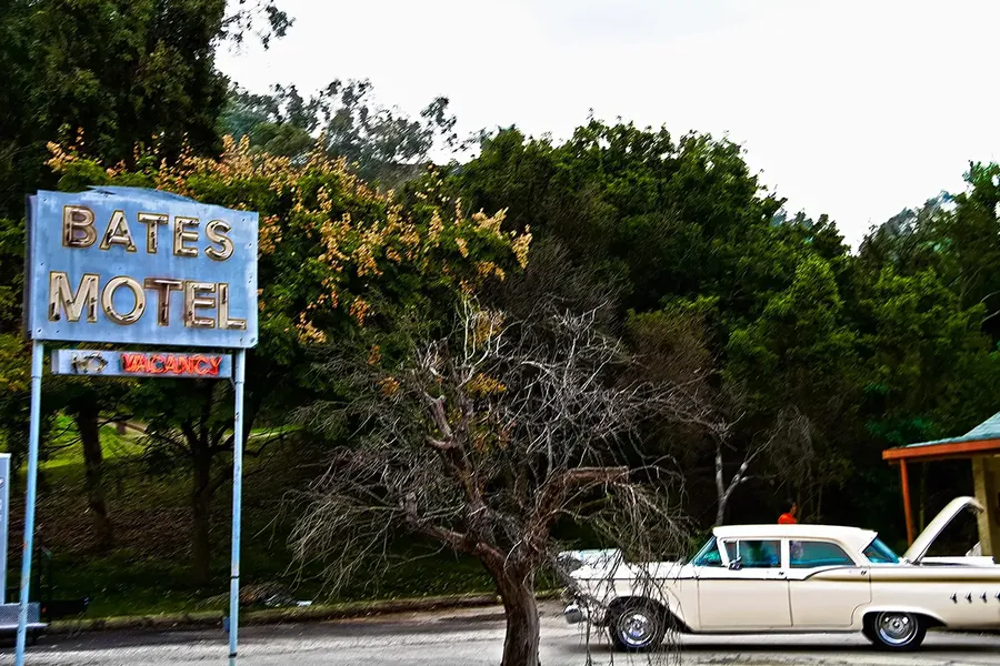 A scene from the hitchcock film, psycho, showing the bates motel sign and a white cadillac with it's boot open in front of the motel