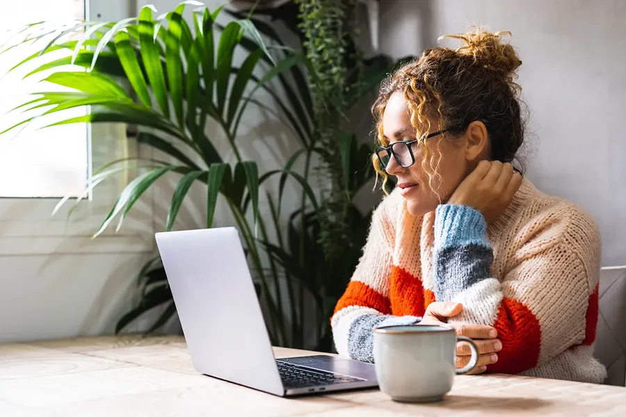 young woman sat at her desk next to a window, with a cup of tea, looking at her laptop reading an example conveyancing quote to understand how much her conveyancing will cost