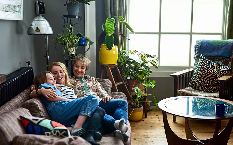 Grandmother, mother and daughter sitting on a sofa together in a living room chatting and smiling