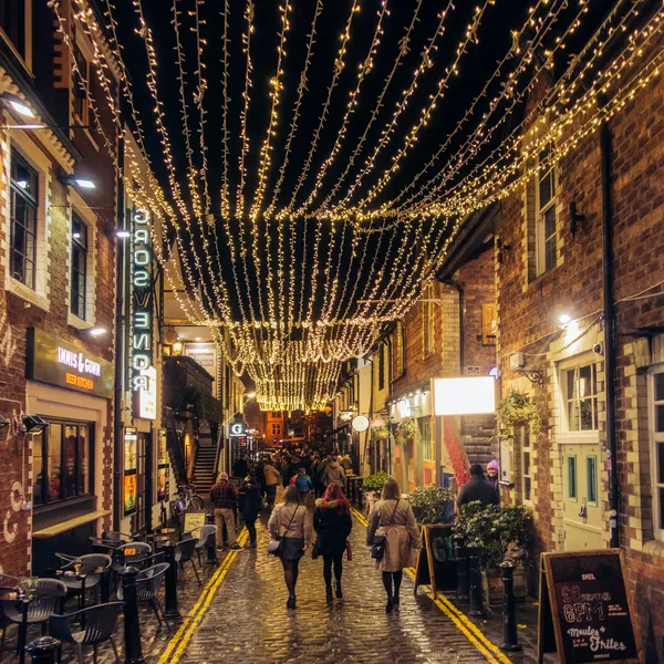 Ashton lane in glasgows west end lit up at night with fairy lights and people walking along it on a night out