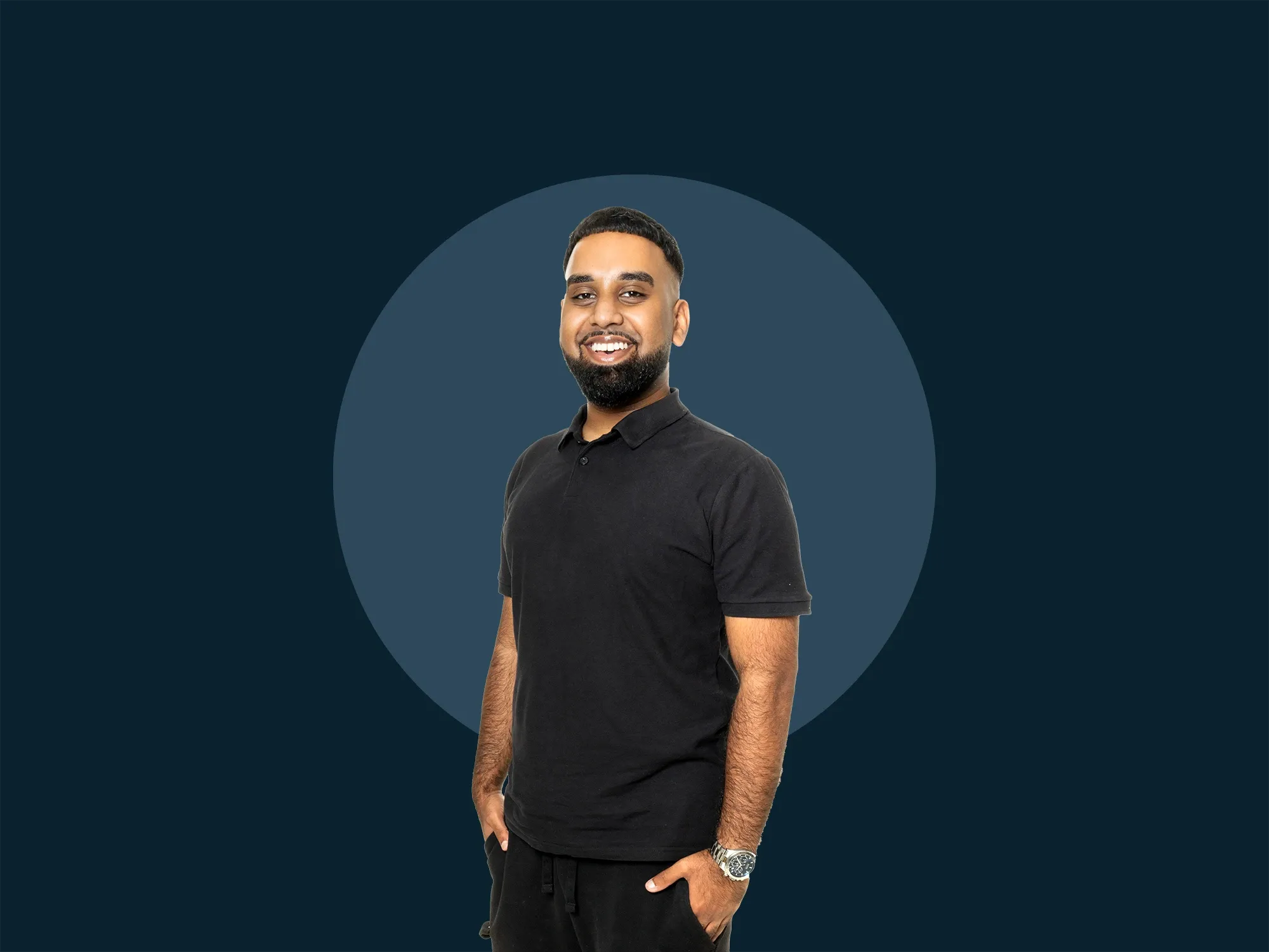 Umar Mansoor in black polo shirt and pants, standing with hands in pockets against a dark background with a circular gradient.