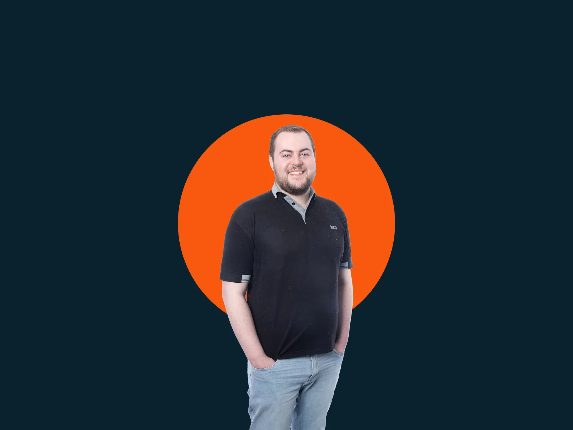 Smiling man in a black polo and jeans stands with hands in pockets on a dark background with a large orange circle.
