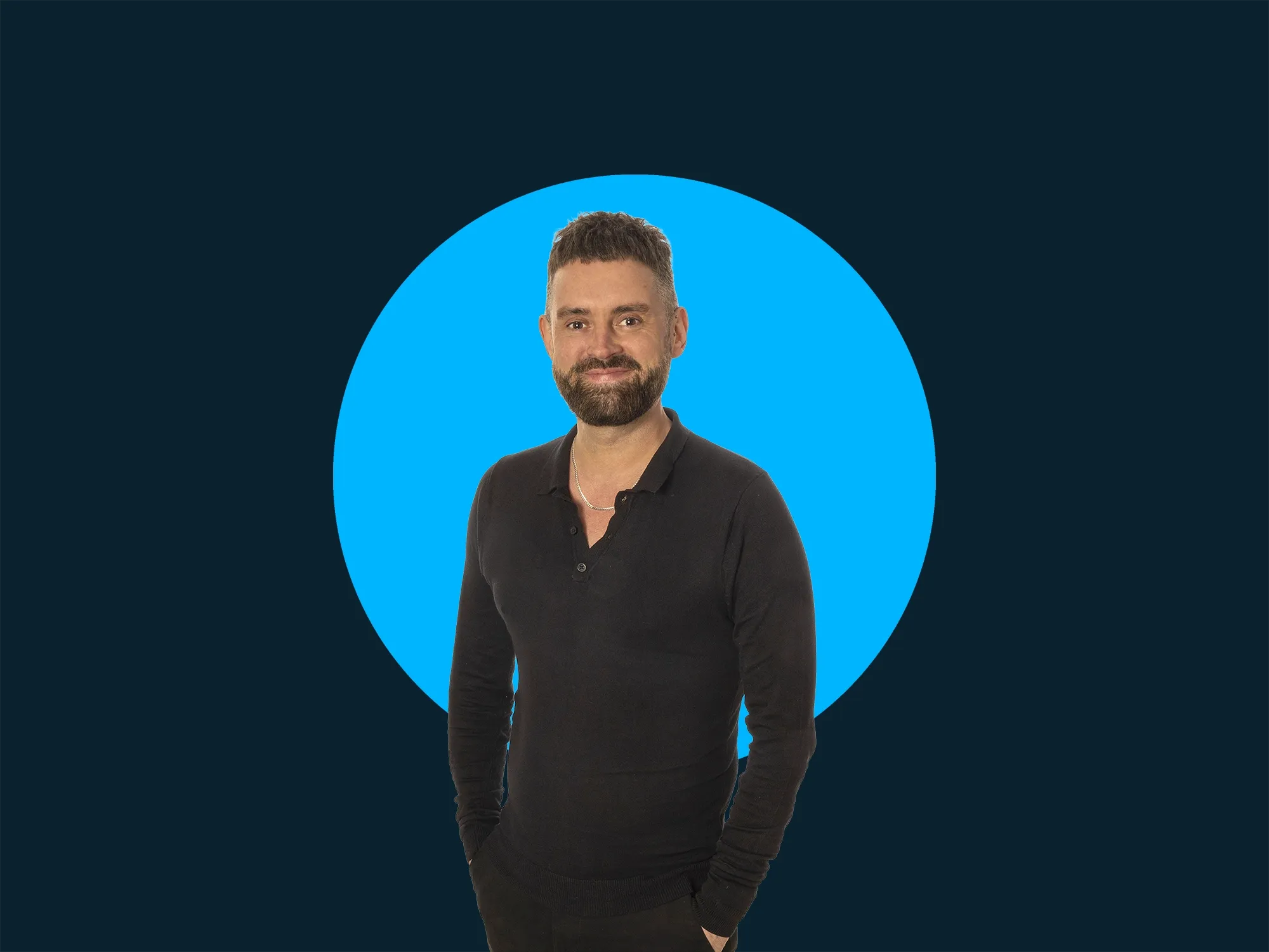 A person with a beard, wearing a black long-sleeve shirt, standing in front of a blue circle on a dark background, smiling.