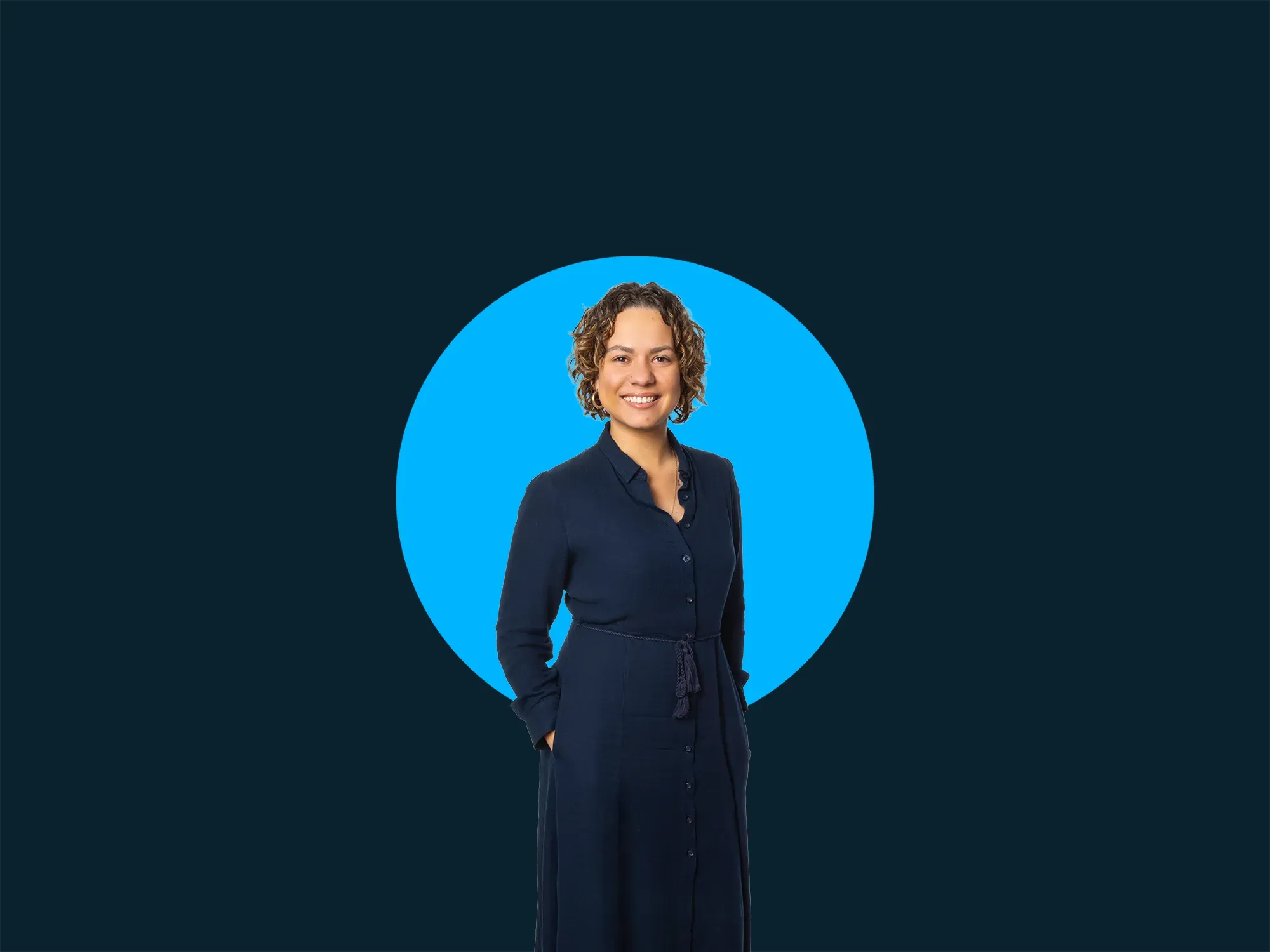 Woman in a navy dress stands smiling against a dark blue background with a bright blue circle behind her.