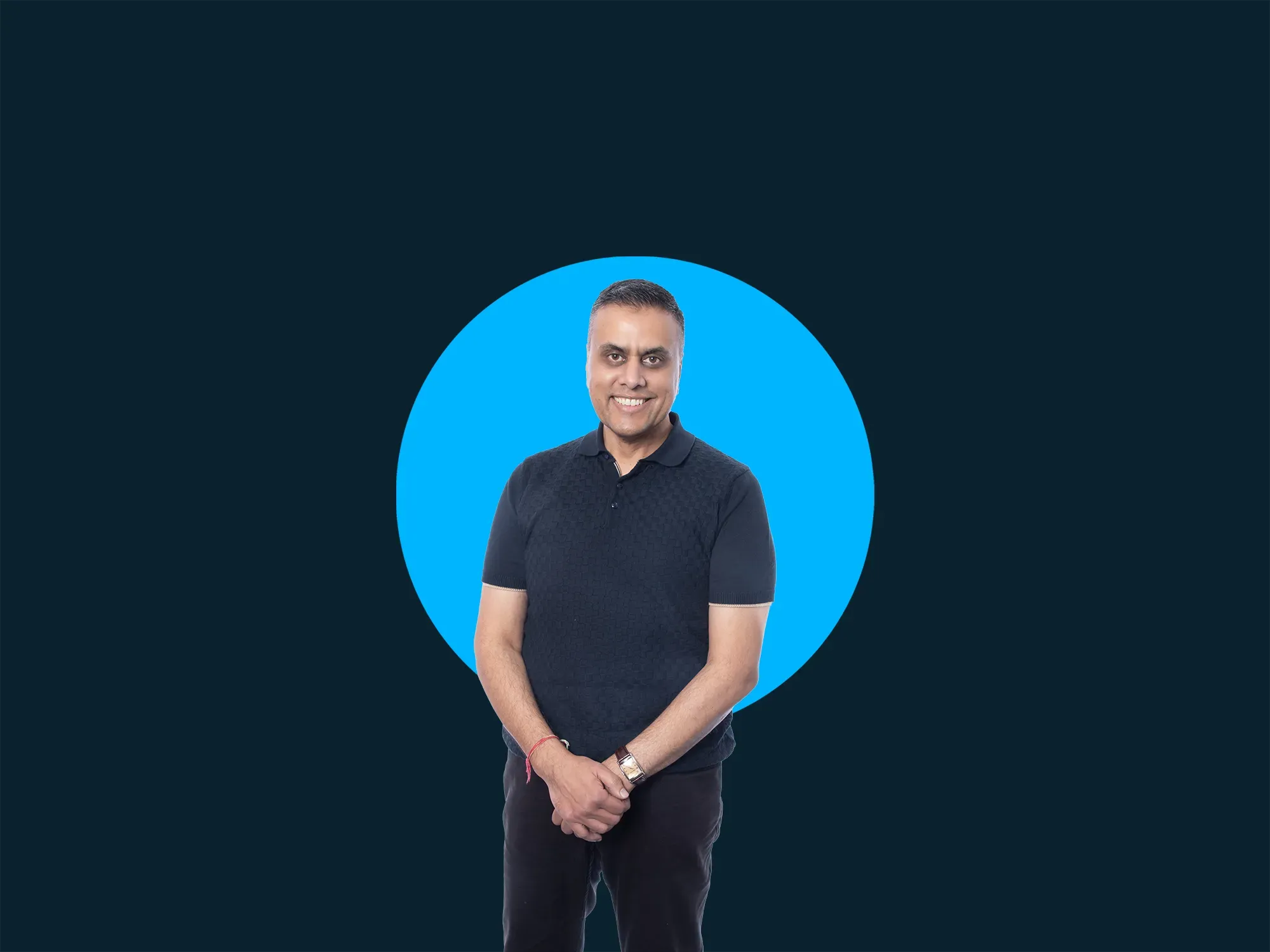 Smiling man in a black shirt stands in front of a blue circle on a dark background.