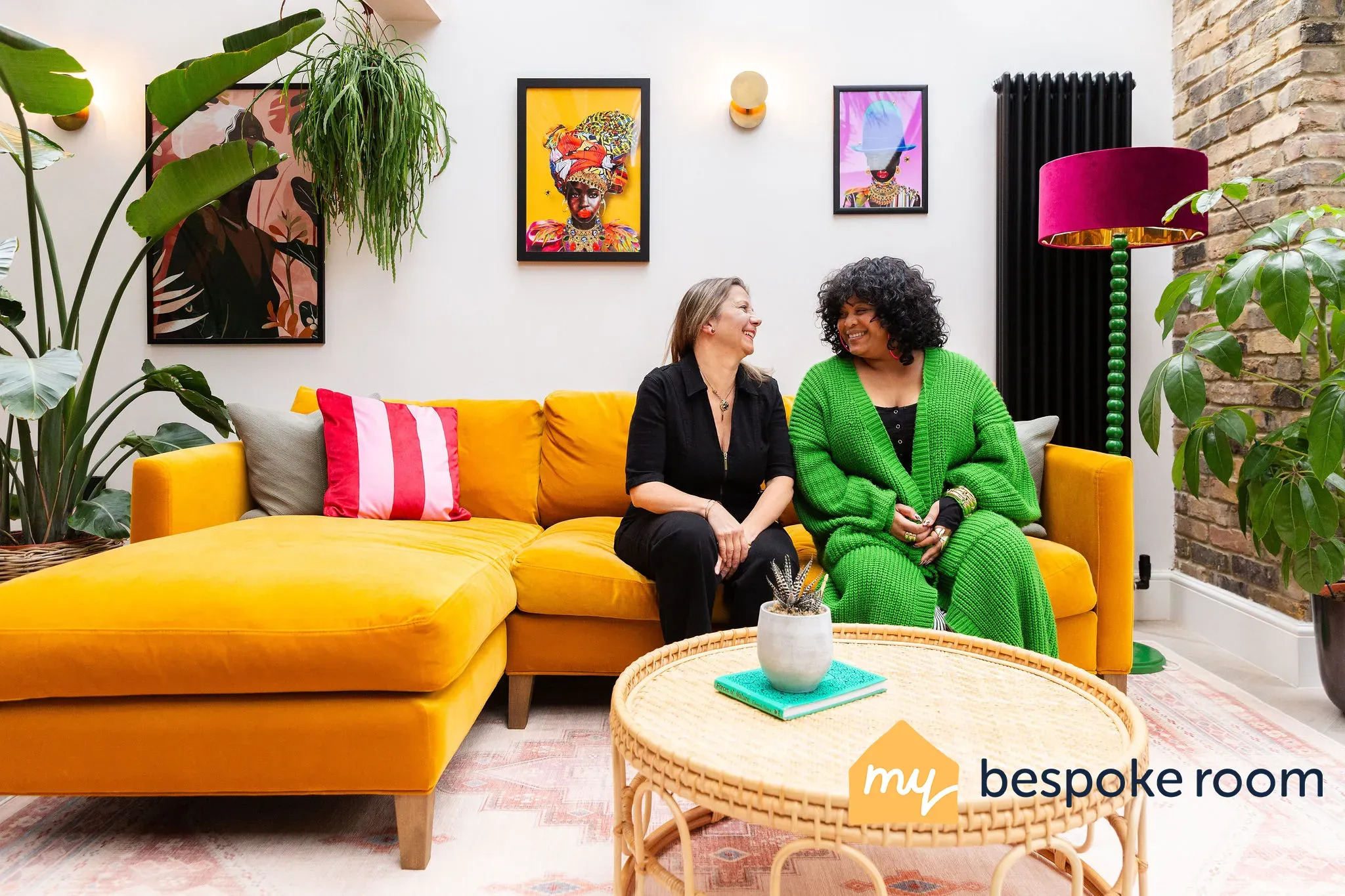 Two people sit on a vibrant yellow sofa in a stylish, plant-filled room. Artwork decorates the walls.