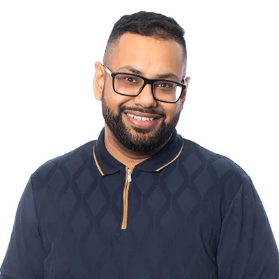 Smiling man with glasses and beard, wearing a navy patterned polo shirt against a white background.