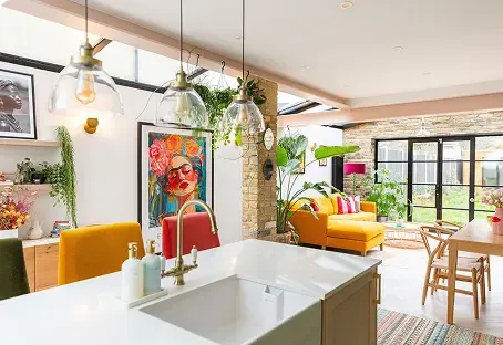 Bright, open-concept living space with modern kitchen, colorful furniture, artwork, pendant lights, and large windows leading to a garden.