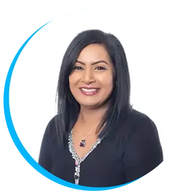 Arti Dhamu smiling with long black hair wearing a dark top and necklace, against a white background with a blue circular border.
