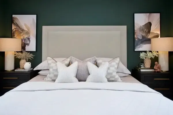 A modern bedroom with a large bed featuring white and gray pillows, flanked by two nightstands with lamps and abstract artwork on the walls.