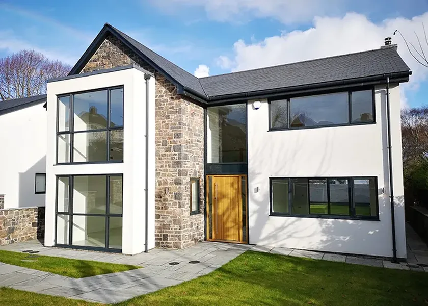 Modern two-story house with stone and white façade, large windows, and a wooden front door, set on a neatly landscaped lawn.
