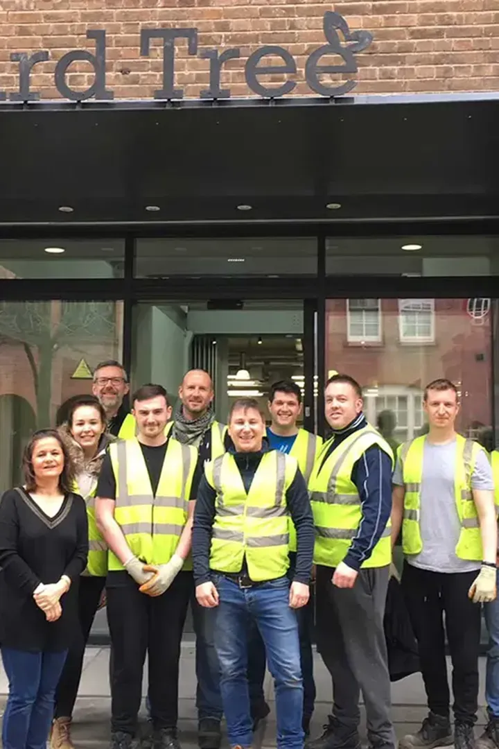 A group of people in safety vests stand smiling in front of a brick building with a glass entrance.