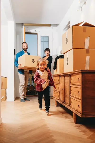 young couple carrying a box through the door of their new home whilst a young girl runs ahead in front of them smiling excitedly