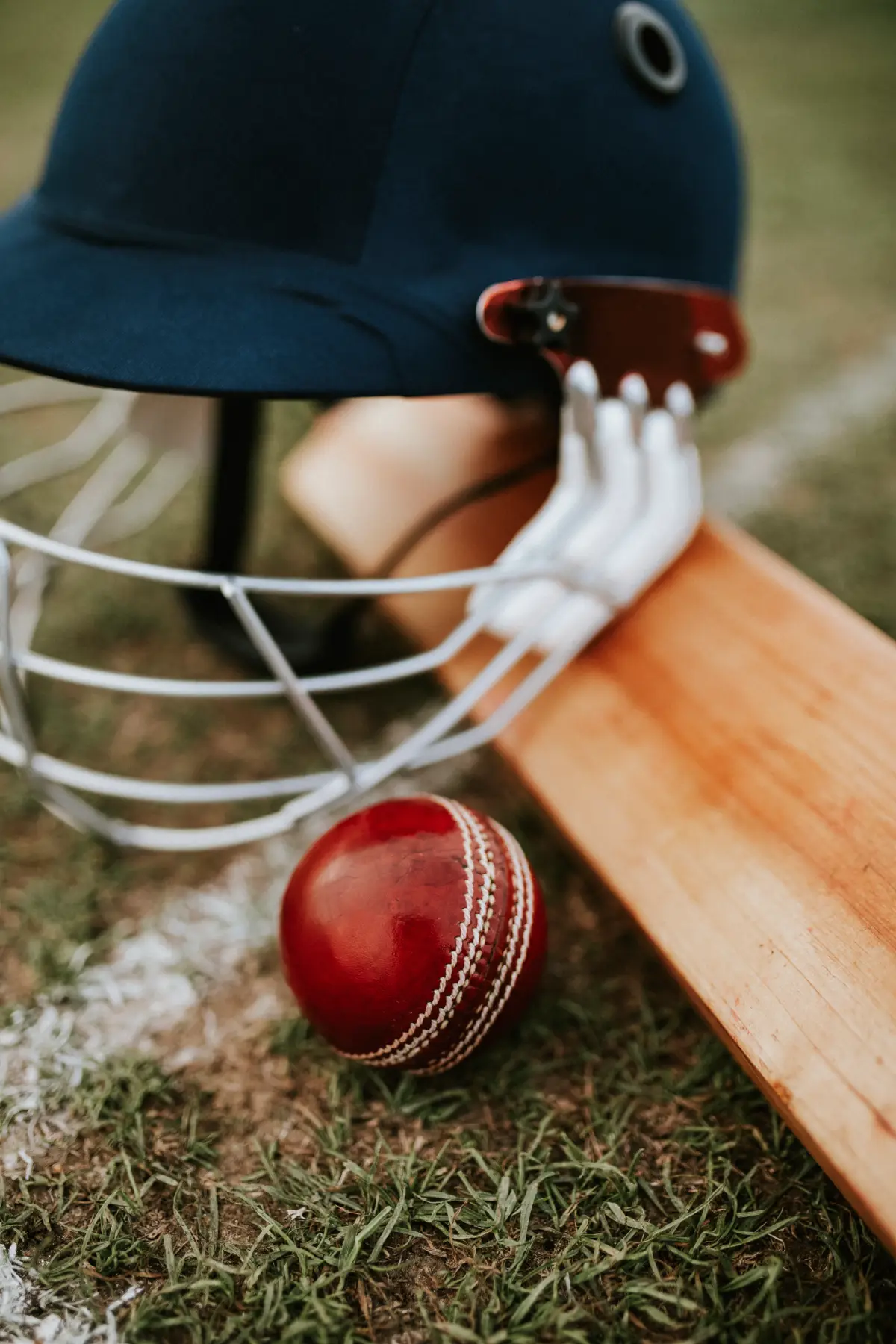 A cricket helmet, bat, and red ball on grass near a boundary line, symbolizing the sport of cricket.