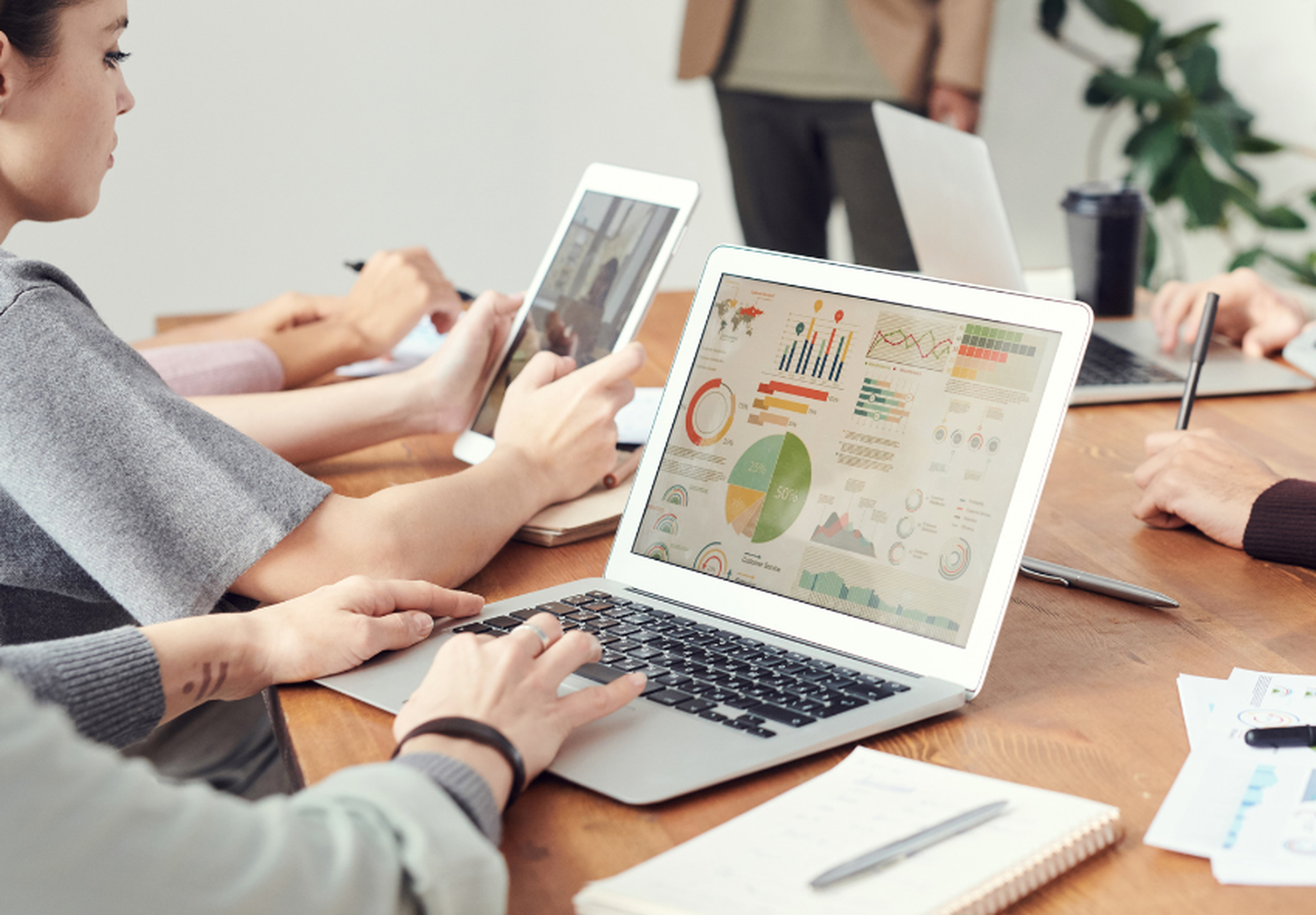 People working at a table with laptops and tablets displaying colorful charts and graphs, engaging in a collaborative meeting.