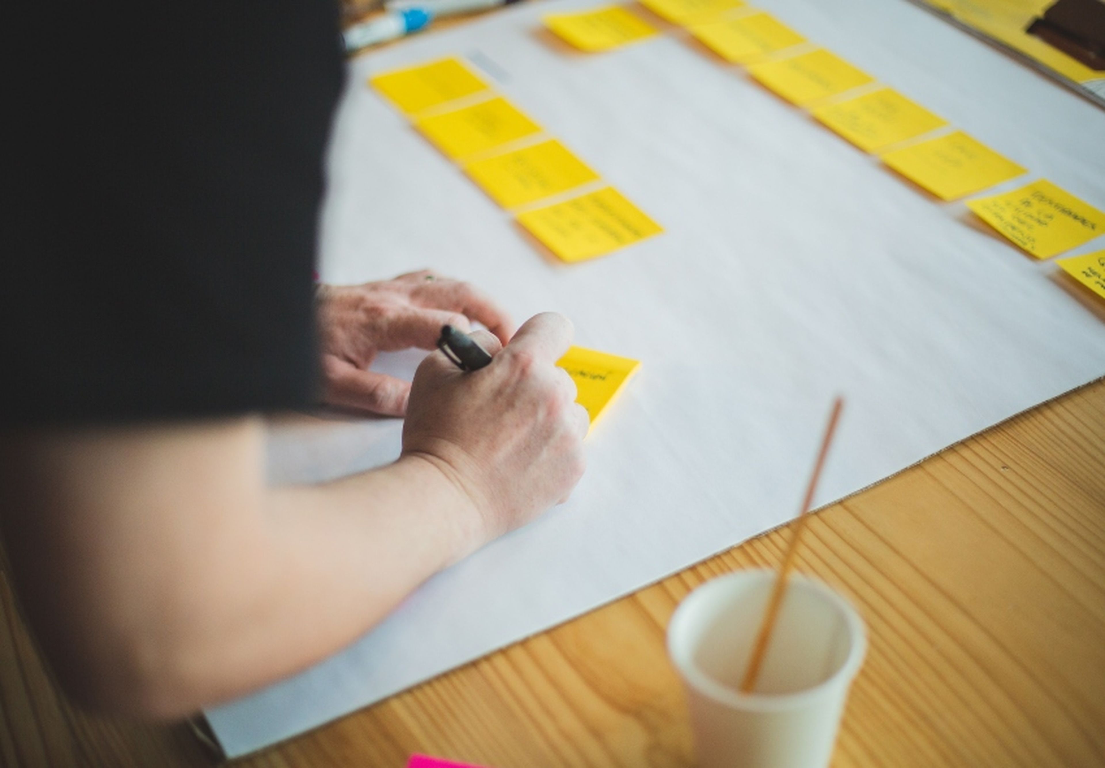 Person writing on sticky notes at a table, with a large sheet of paper and organized notes in the background.