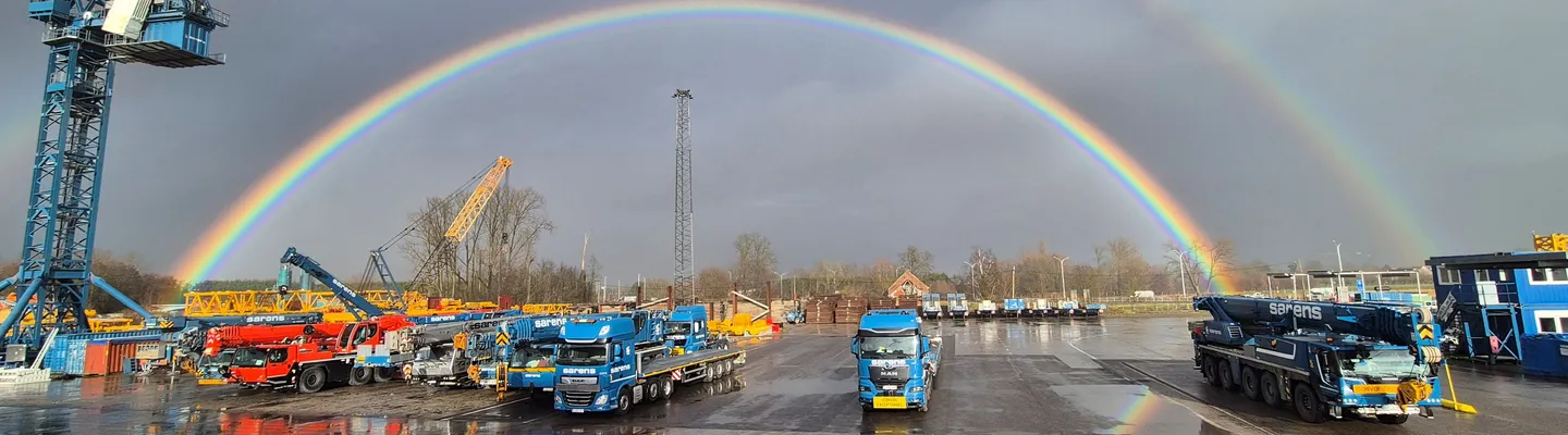 Sarens crane fleet and heavy lifting equipment at the company site beneath a rainbow