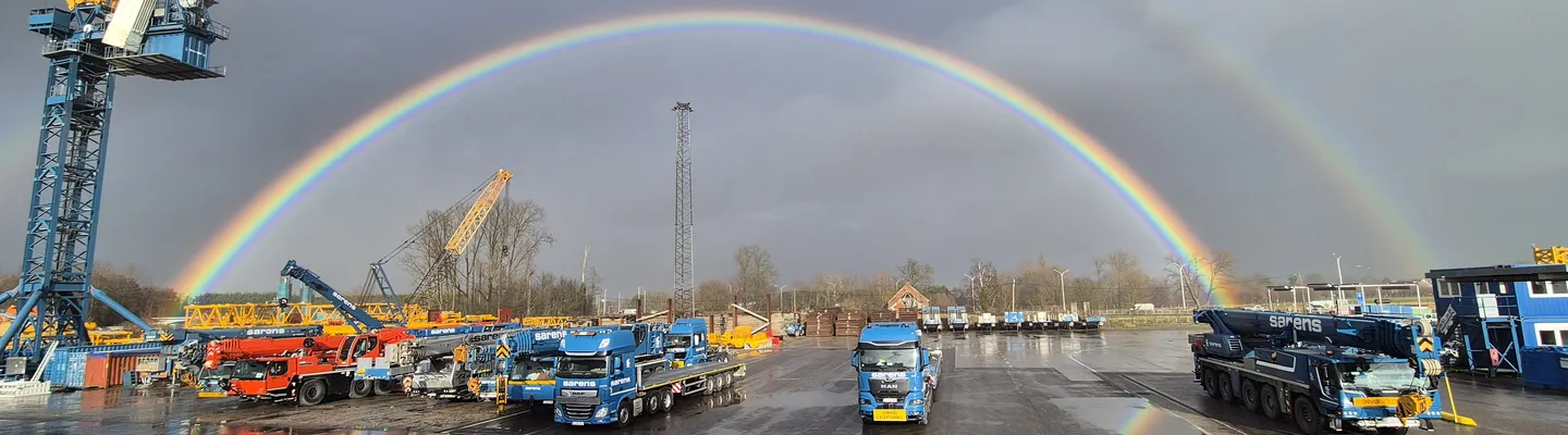 Sarens crane fleet and heavy lifting equipment at the company site beneath a rainbow