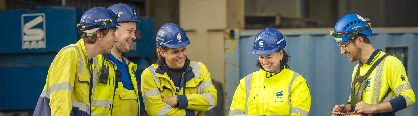 Sarens employee discussing work with colleagues on site while wearing a safety helmet and high-visibility vest