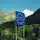 Blaues Straßenschild mit EU-Sternen und der Aufschrift „Republik Österreich“ in einer Berglandschaft mit grünen Hügeln und klarem blauem Himmel.
