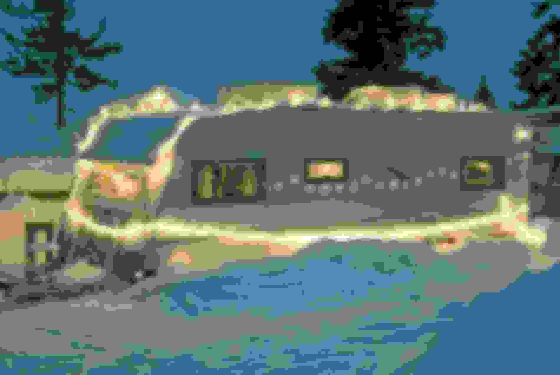 Ein schneebedeckter Camper, geschmückt mit Lichterketten, steht in einer verschneiten Landschaft, umgeben von Bäumen in der Dämmerung.