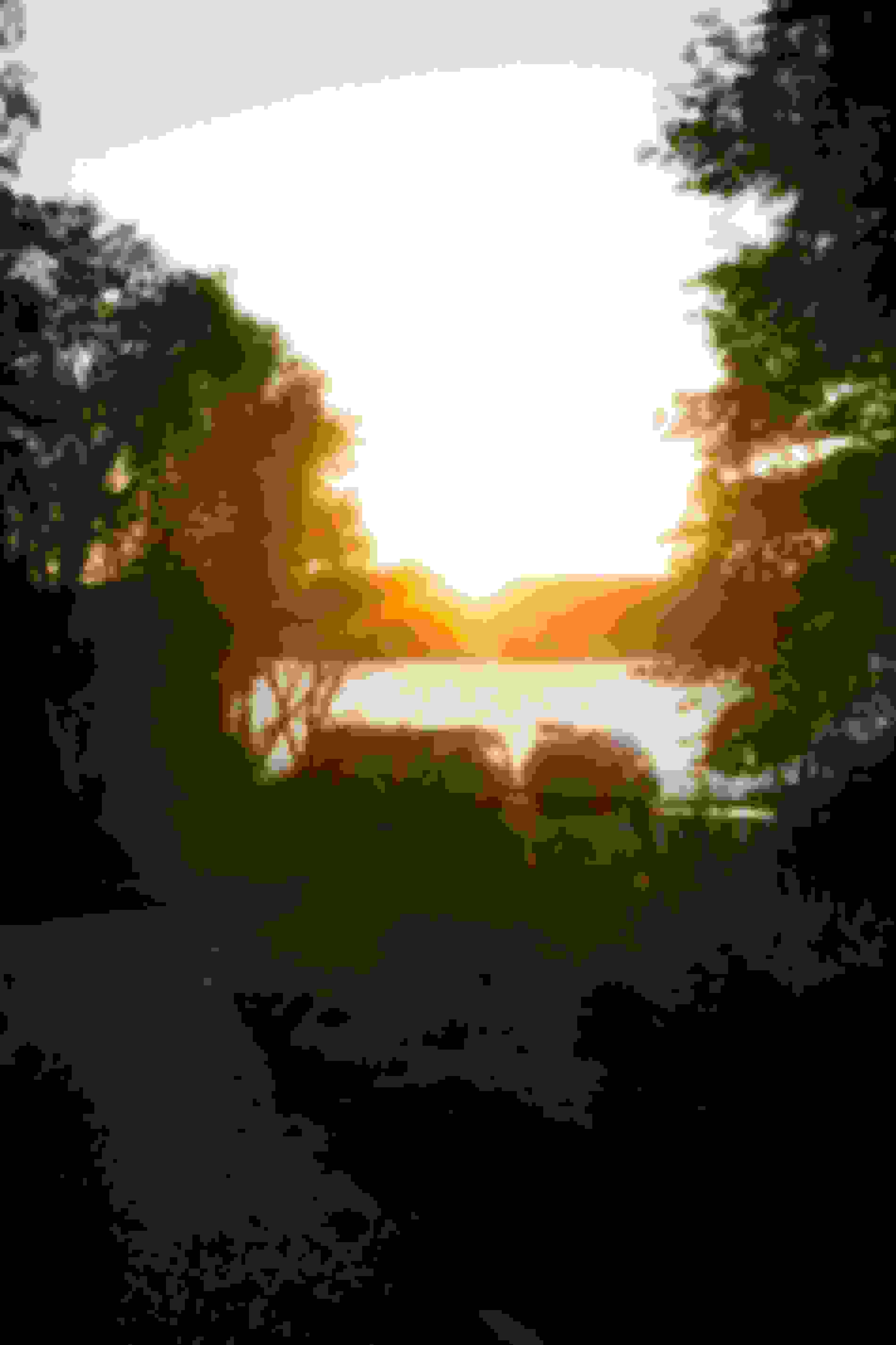 Sonnenuntergang über einem See mit zwei Campervans am Ufer, umgeben von Bäumen und einer sich schlängelnden Straße im Vordergrund.
