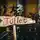 Holzschild in Pfeilform mit dem roten Schriftzug „Toilette“, vor einem Hintergrund aus Pflanzen und orangefarbenen Wänden.