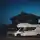 Ein weißes Wohnmobil steht in der Abenddämmerung auf einer ruhigen Straße vor einem im Schatten liegenden Haus, unter einem tiefblauen Himmel.