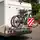 Ein Wohnmobil steht am Straßenrand, auf einem Heckträger sind zwei Fahrräder befestigt. Daran ist ein rot-weißes Warnschild angebracht, im Hintergrund sind Bäume zu sehen.