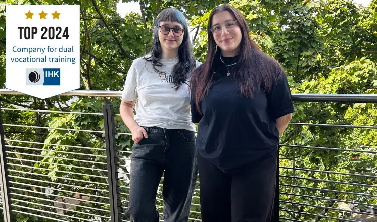 The company’s two apprentices standing together on a balcony; on the left, the IHK seal ‘Top 2024 Company for dual vocational training’.