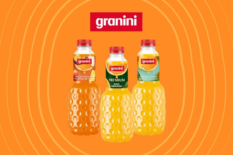 Three Granini juice bottles—Fruit Cocktail, 100% Orange, and Orange Mango—on an orange background with concentric circles.