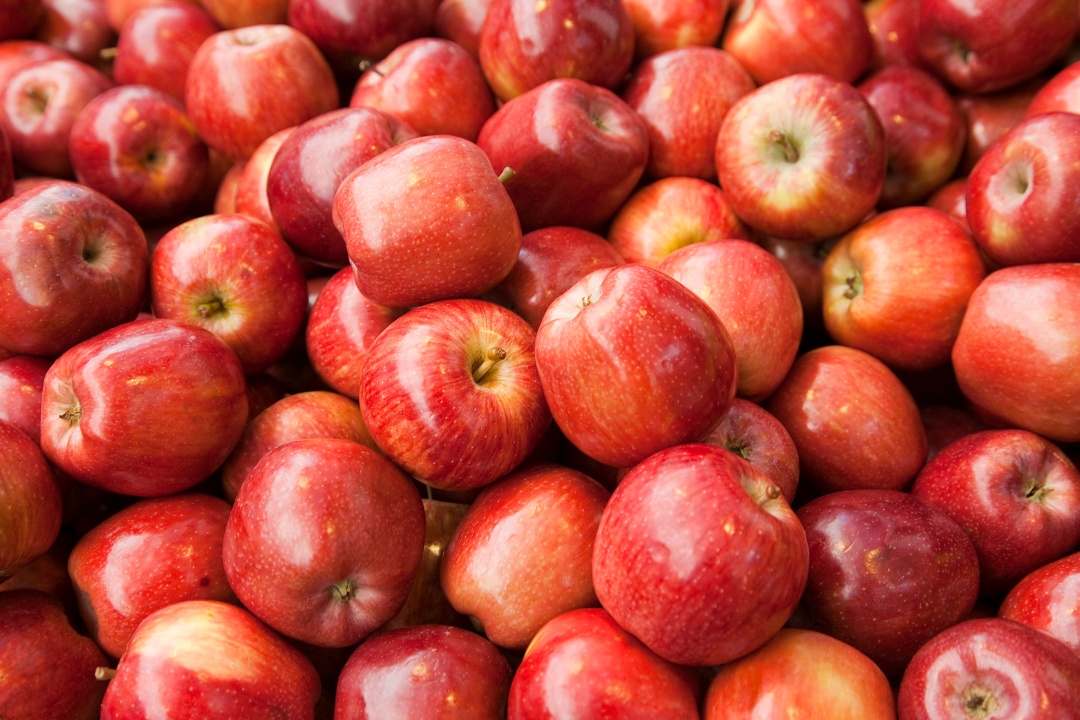 A pile of fresh red apples with shiny skins, varying in shades from bright red to deep crimson, filling the entire frame.