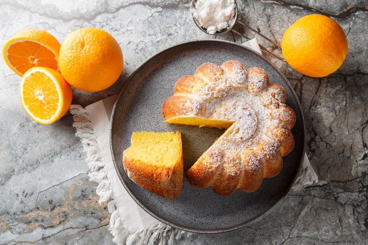 Lemon cake on a grey plate with oranges on the side on a marbled surface