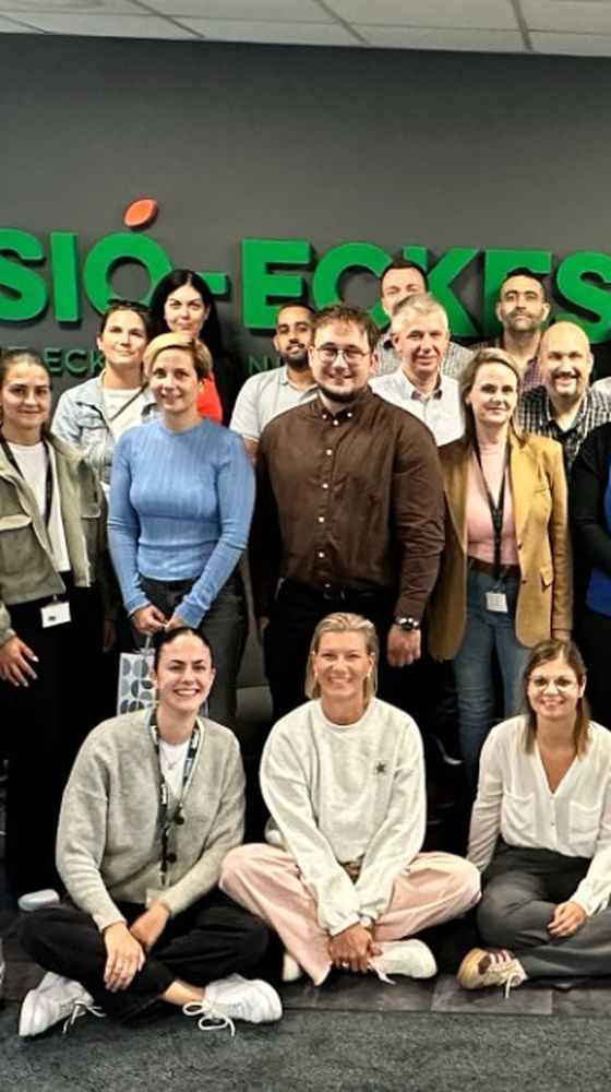 A group of people posing for a photo in an office setting with the "Sió-Eckes" sign behind them.