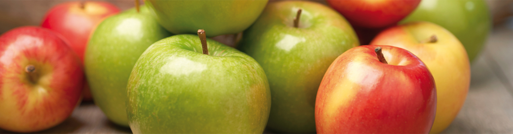 A pile of red and green apples on a wooden surface, with a focus on their shiny, smooth skins.