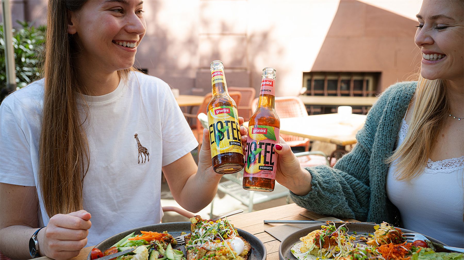 Bottle of iced tea on a wooden table with a woman eating a salad in the background.
