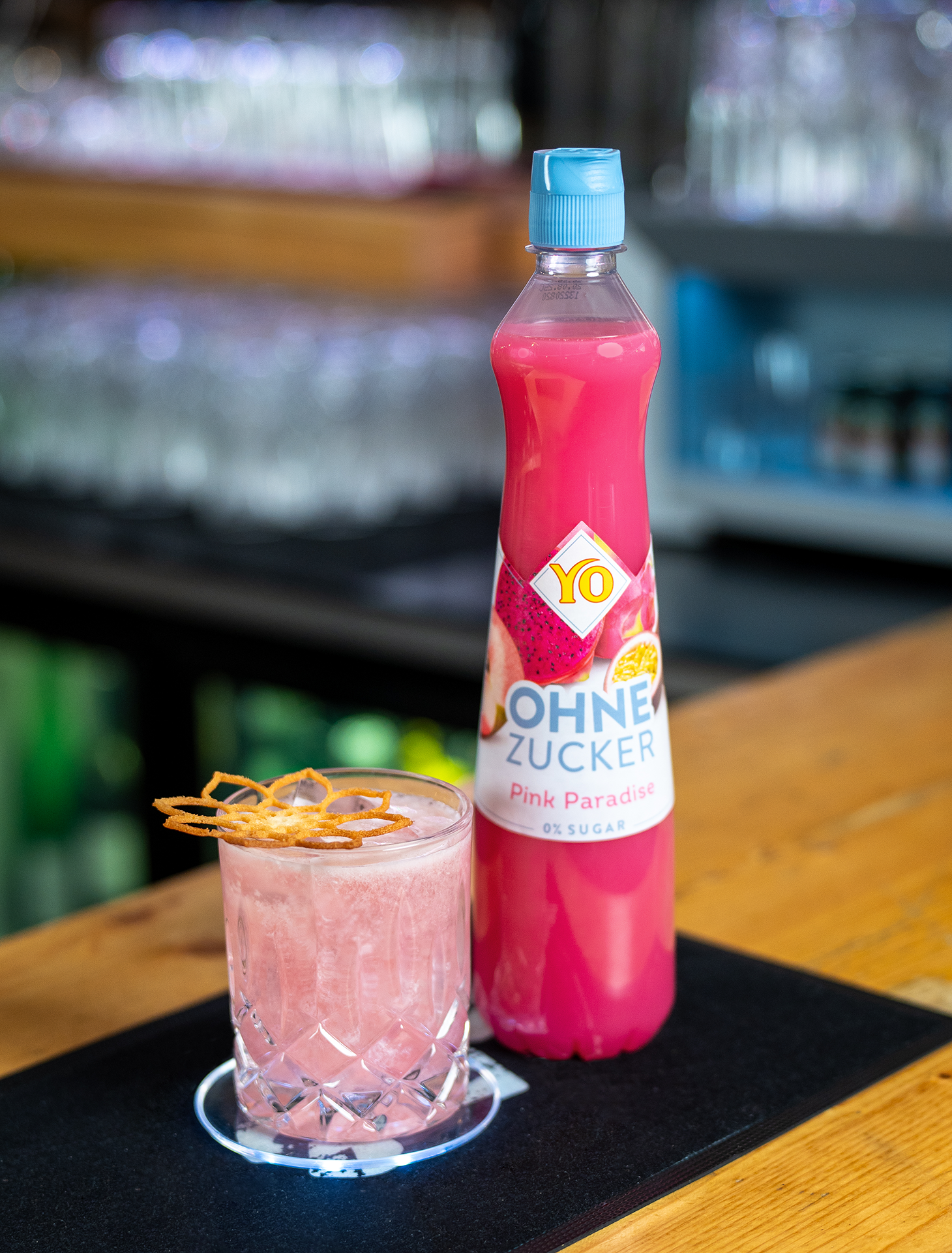 Cocktail "Auroras Kiss" in einem Glas und daneben die Flasche YO Pink Paradise.