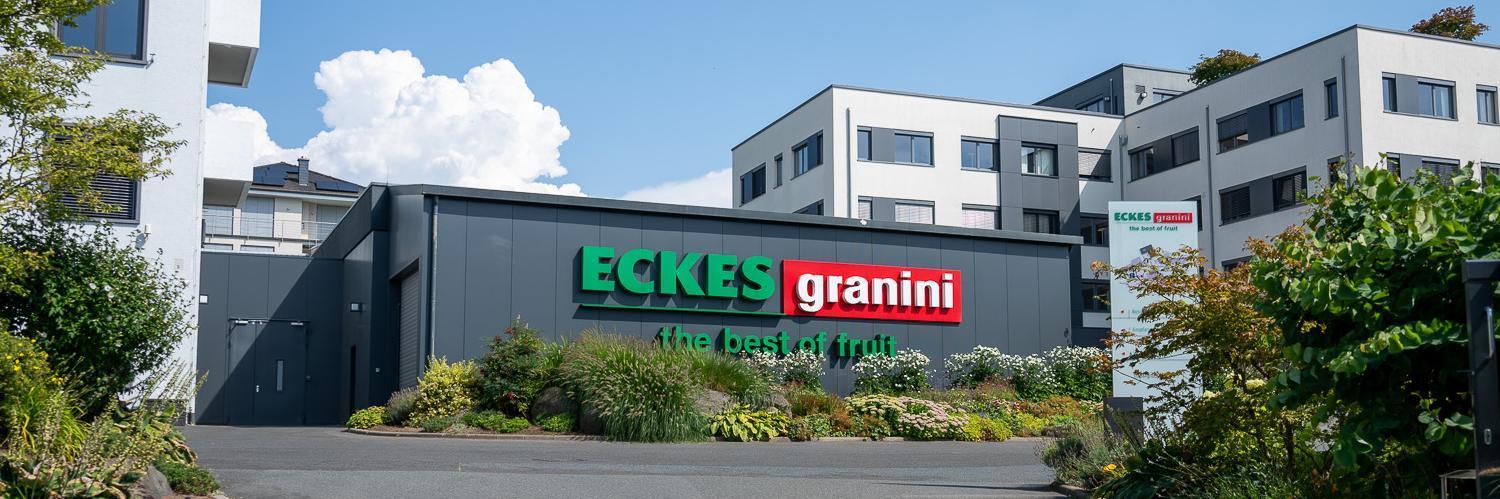 Modern office buildings with "Eckes Granini" signage, surrounded by landscaped greenery and clear blue sky with clouds.