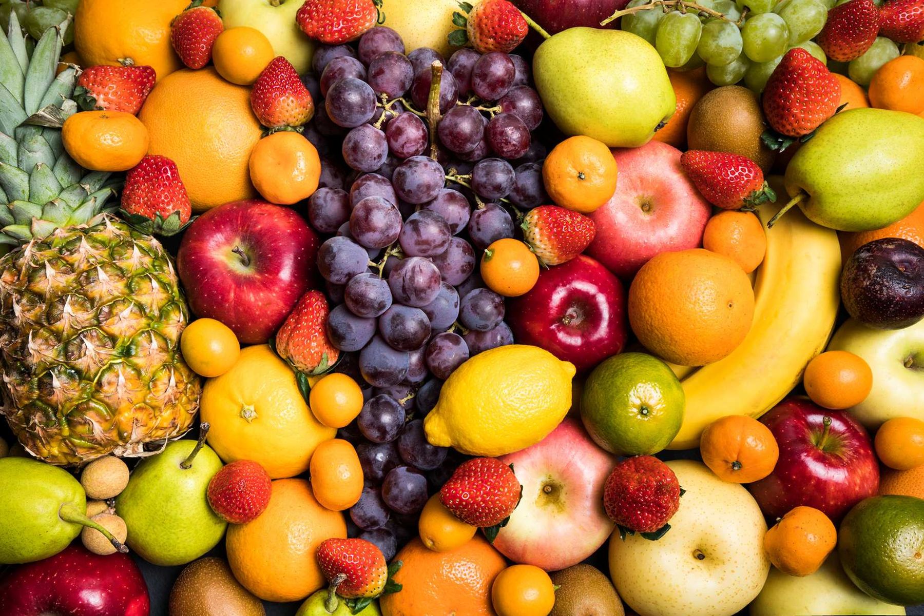 A colorful assortment of fruits including grapes, strawberries, apples, oranges, bananas, and a pineapple, arranged closely together.