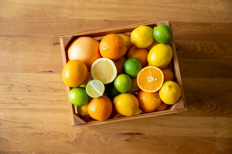 Holzkiste mit Orangen, Limette, Grapefruit und Zitronen auf Holzplatte von granini