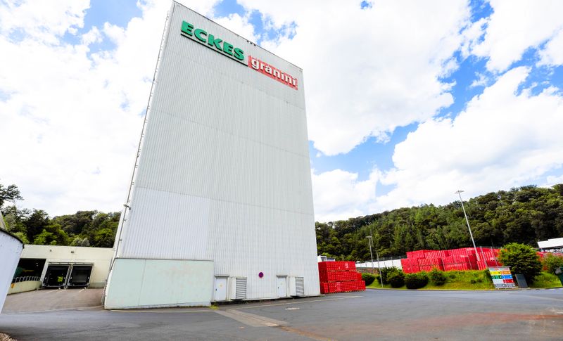 Factory Broel: A tall white industrial building with "Eckes granini" signage, surrounded by greenery and red crates under a partly cloudy sky.