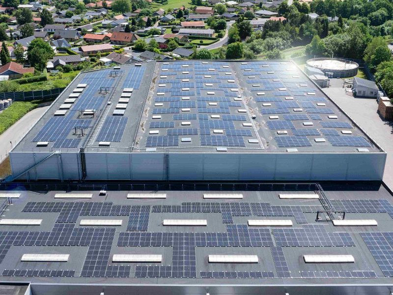 Rooftop solar panels on a large building in a suburban area with houses and greenery in the background.