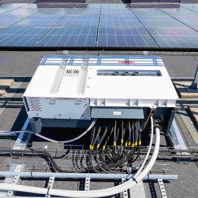 Solar panels on a roof with electrical cables connected to a white inverter system, under bright sunlight.