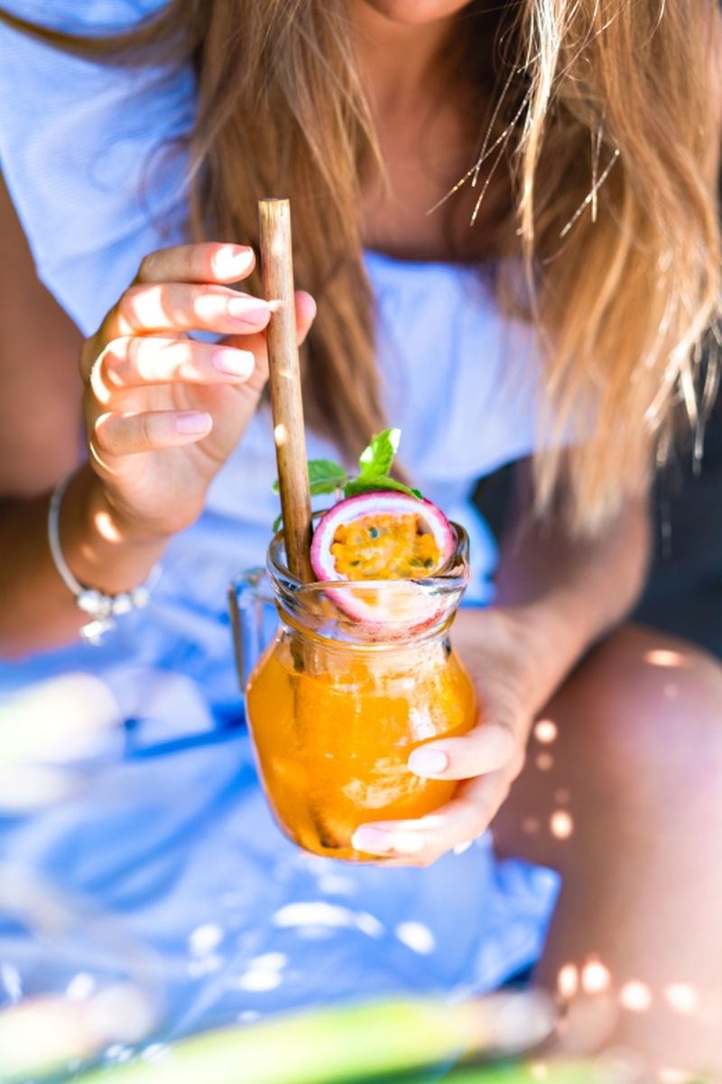 Cocktail mit Maracuja im Glas, gehalten von einer Frau draußen im Sonnenschein