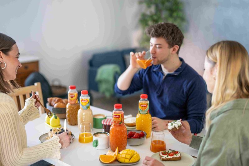 Breakfast setting with four granini juices, a man is drinking juice, the other two girls are smiling and eating