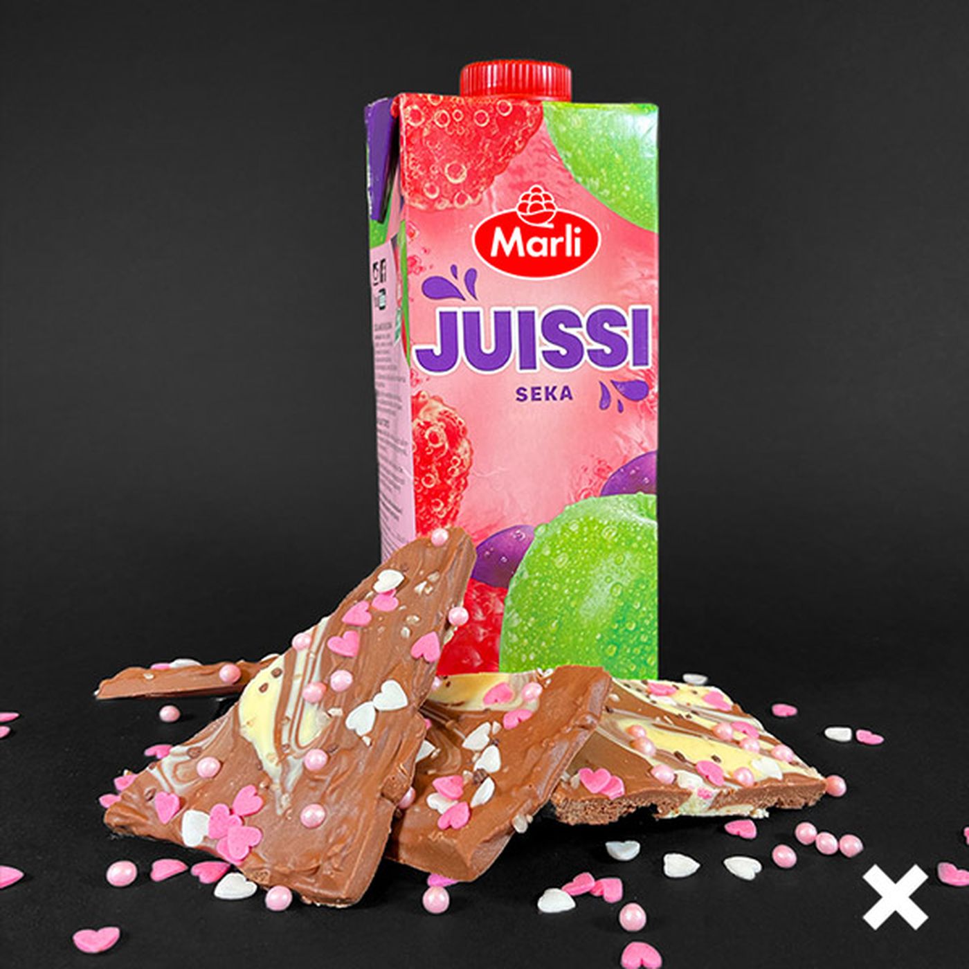A carton of Marli Juissi fruit juice is placed behind pieces of chocolate topped with pink and white heart-shaped sprinkles.